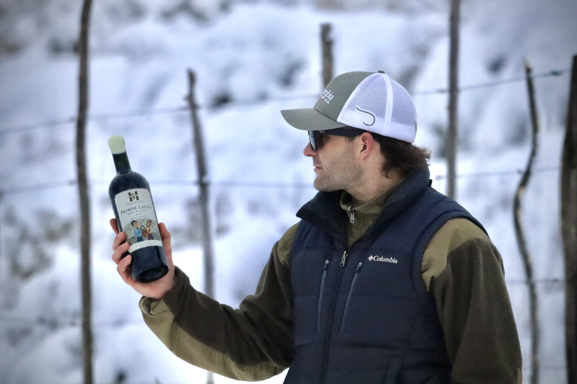 Persona sosteniendo una botella de Primer Latido en un viñedo nevado